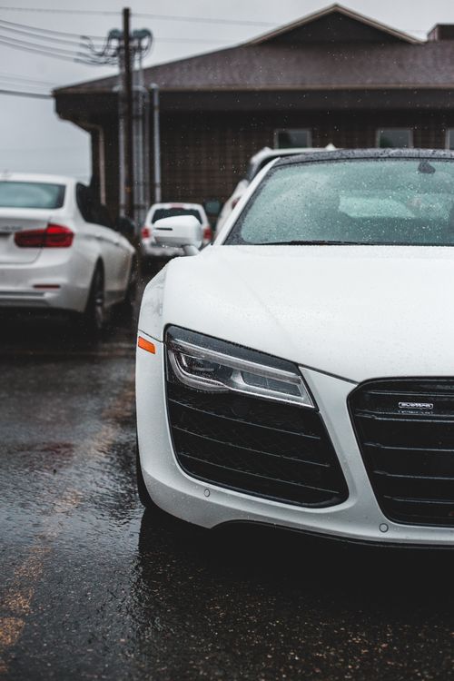 Free Front bumper of contemporary sports auto with wet surface parked on asphalt pavement near building Stock Photo