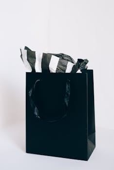 Elegant black shopping bag with striped tissue paper against a white background.