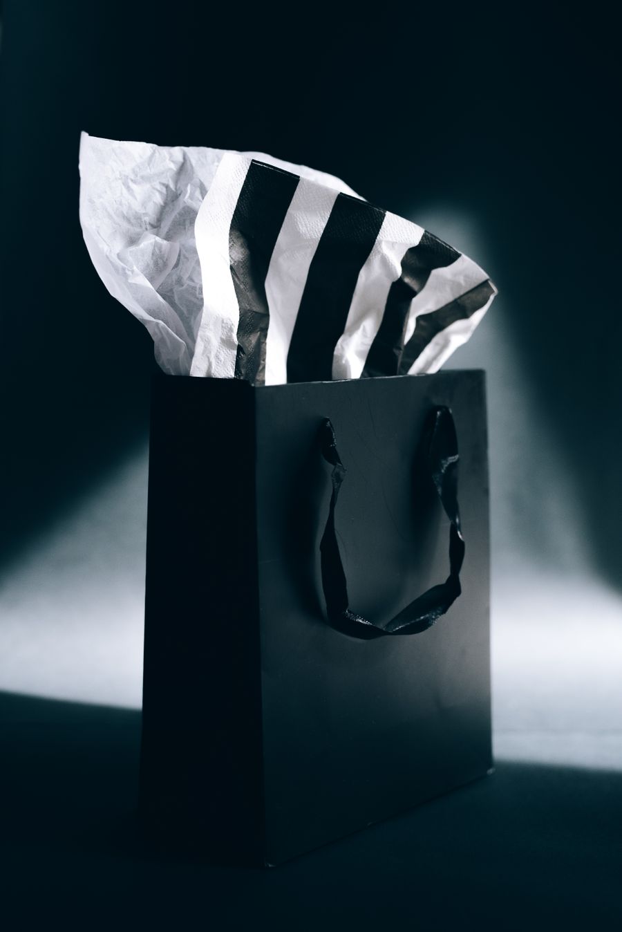 A black boutique bag with ribbon handles lit against a dark background