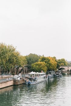 船只停靠在巴黎塞纳河上，四周环绕着郁郁葱葱的绿化和历史悠久的桥梁，呈现出一片宁静的景象