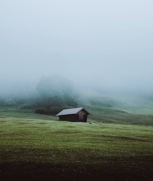 Brown Wooden House on Green Grass Field Covered With Fog