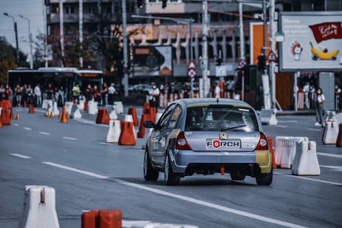 Modern silver car driving on street with traffic cones