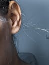 Closeup of ear with trace of puncture and hair of crop anonymous woman near wall in dark room