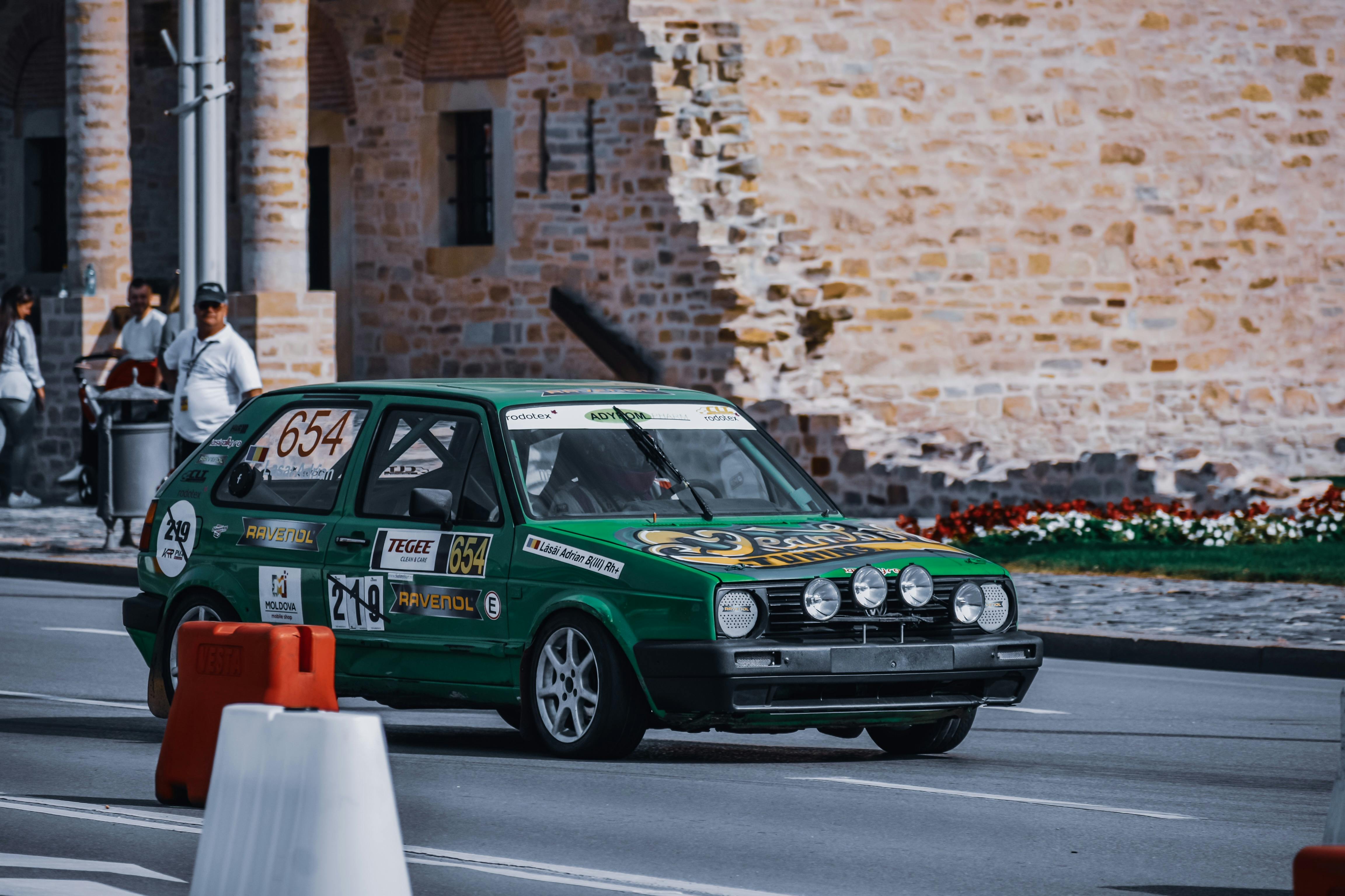 Free Old green automobile moving on asphalt road near pavement with people and aged brick building with columns Stock Photo