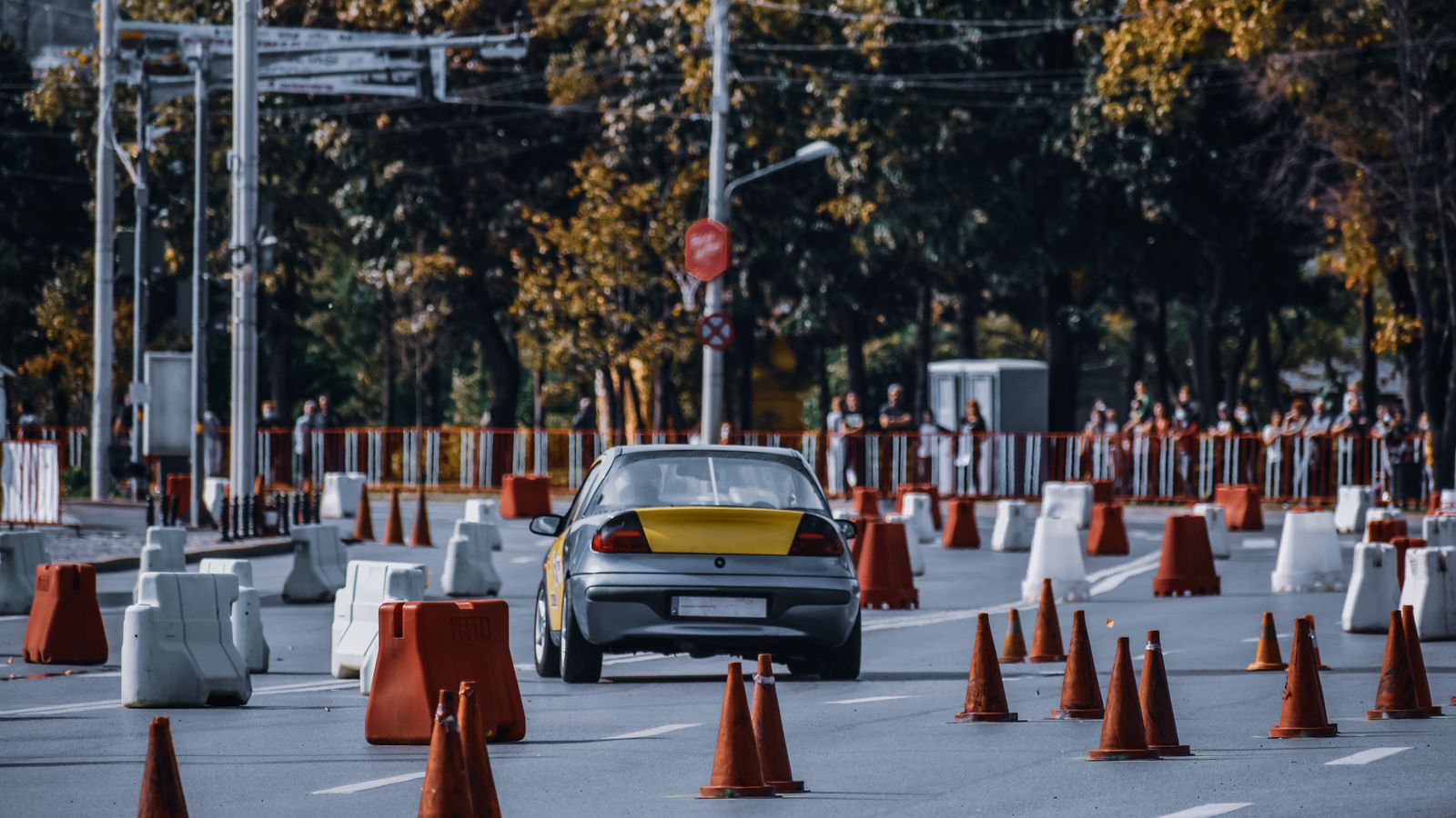 Participant in car race maneuvering between red and white traffic cones or barriers in front of audience