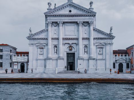 Tourists walking on square in front of San Giorgio church decorated with columns and sculptures on Grand canal in Venice Italy