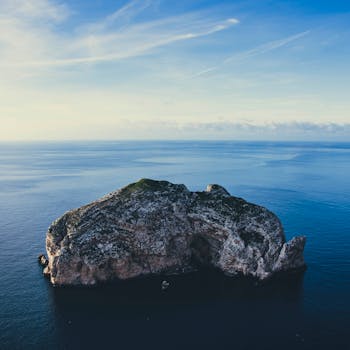 Captivating aerial view of a solitary rock formation in the vast ocean under a clear sky.
