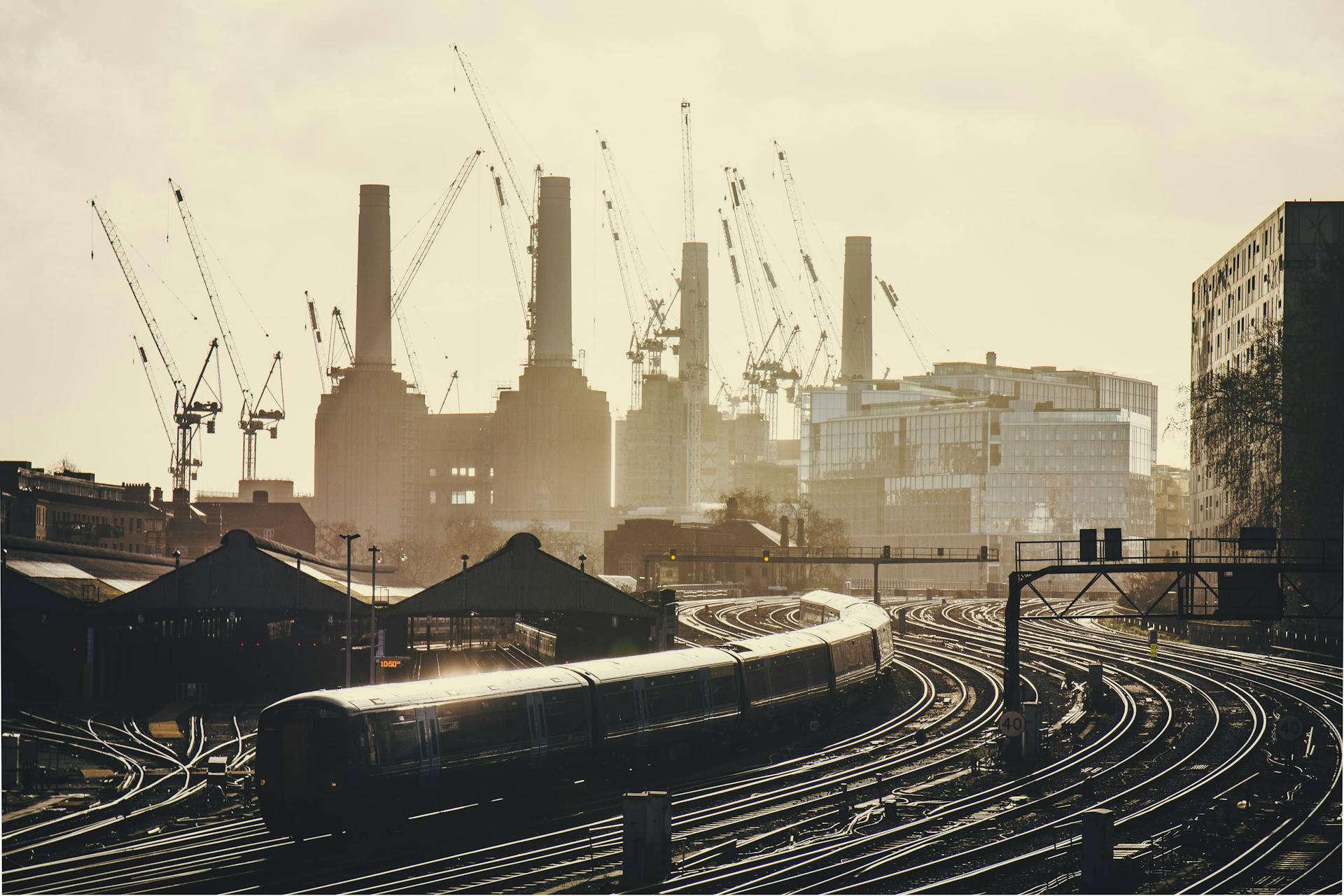 A busy urban railway with train tracks and cranes set against a modern industrial skyline.