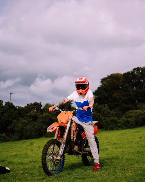 Man Riding an Orange Motorcycle on Green Grass Field 
