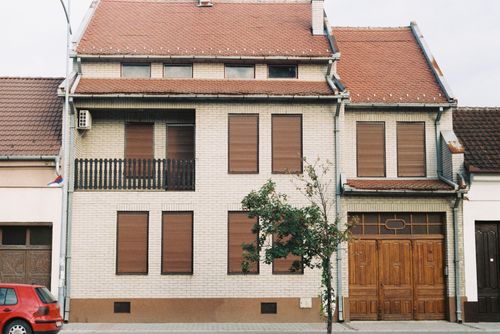 Free Brick house with brown shutters and garage, featuring a tree in front on a quiet street. Stock Photo