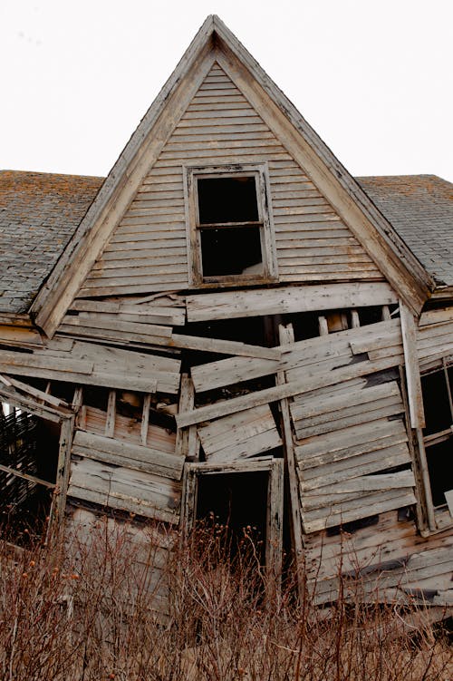 Weathered lumber shed with broken walls and rusty roof located in grassy countryside