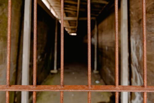 Aged shed with long corridor between rough walls near rusty fence in daytime