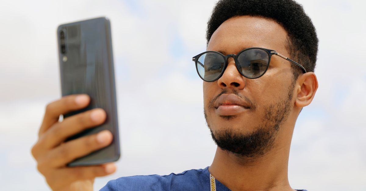Close-up de um homem africano usando óculos de sol e um smartphone ao ar livre em Mogadíscio, Somália.