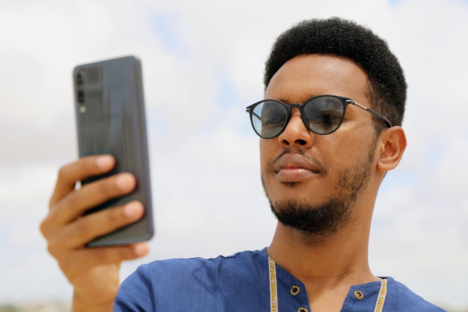 Close-up of an African man wearing sunglasses and using a smartphone outdoors in Mogadishu, Somalia.