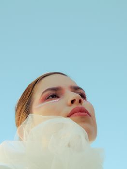 一位妆容明亮的年轻女性站在蓝天下，目光移向别处