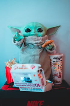 Plastic toy anime figure with chicken cutlet near fast food box and French fries at home