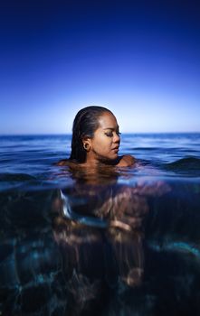 Young ethnic female traveler with dark wet hair relaxing in rippling sea water during summer holidays