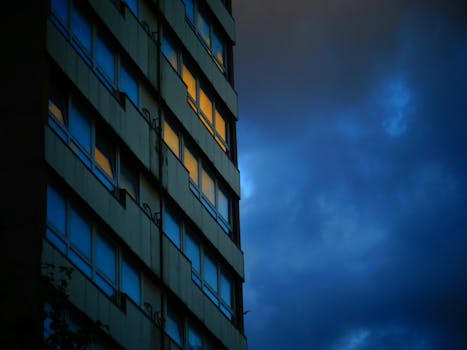 在夜间多云天空下，现代城市建筑呈现低角度视图，窗户明亮
