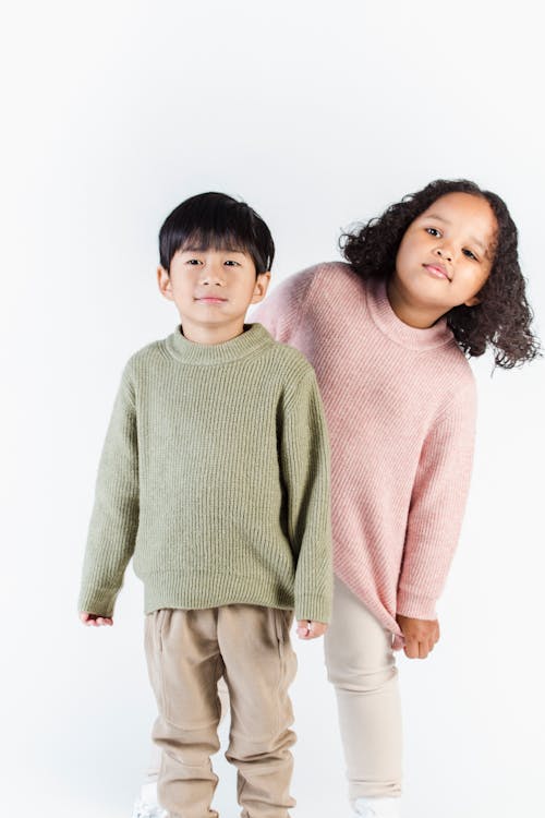 Little diverse cute kids wearing warm knitted sweaters and pants standing against white background