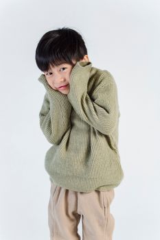 一个穿着舒适绿色毛衣的迷人孩子，害羞地站在白色背景前