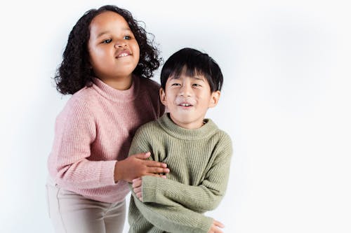 Smiling multiethnic children wearing knitted soft sweaters cuddling in studio against white background