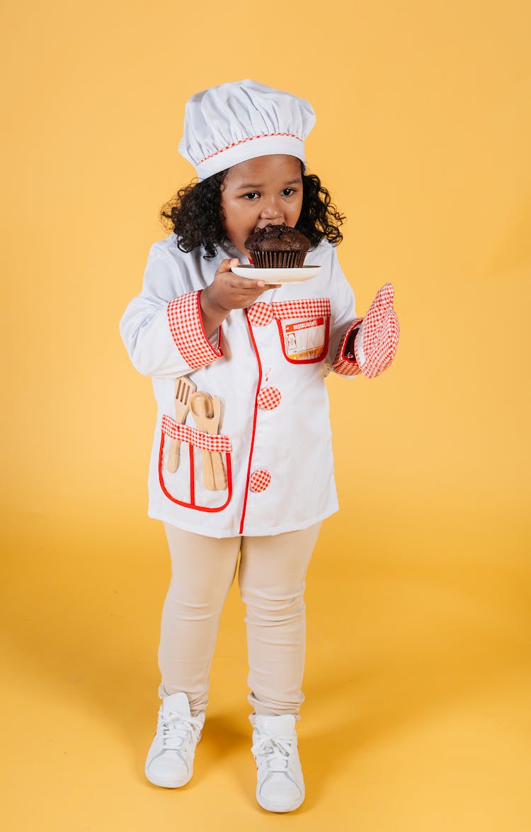 Little Black Girl Biting Chocolate Muffin On Plate