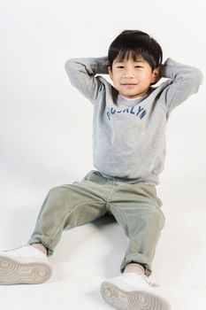 一个穿着时尚休闲服装的可爱亚洲小男孩坐在工作室的地板上