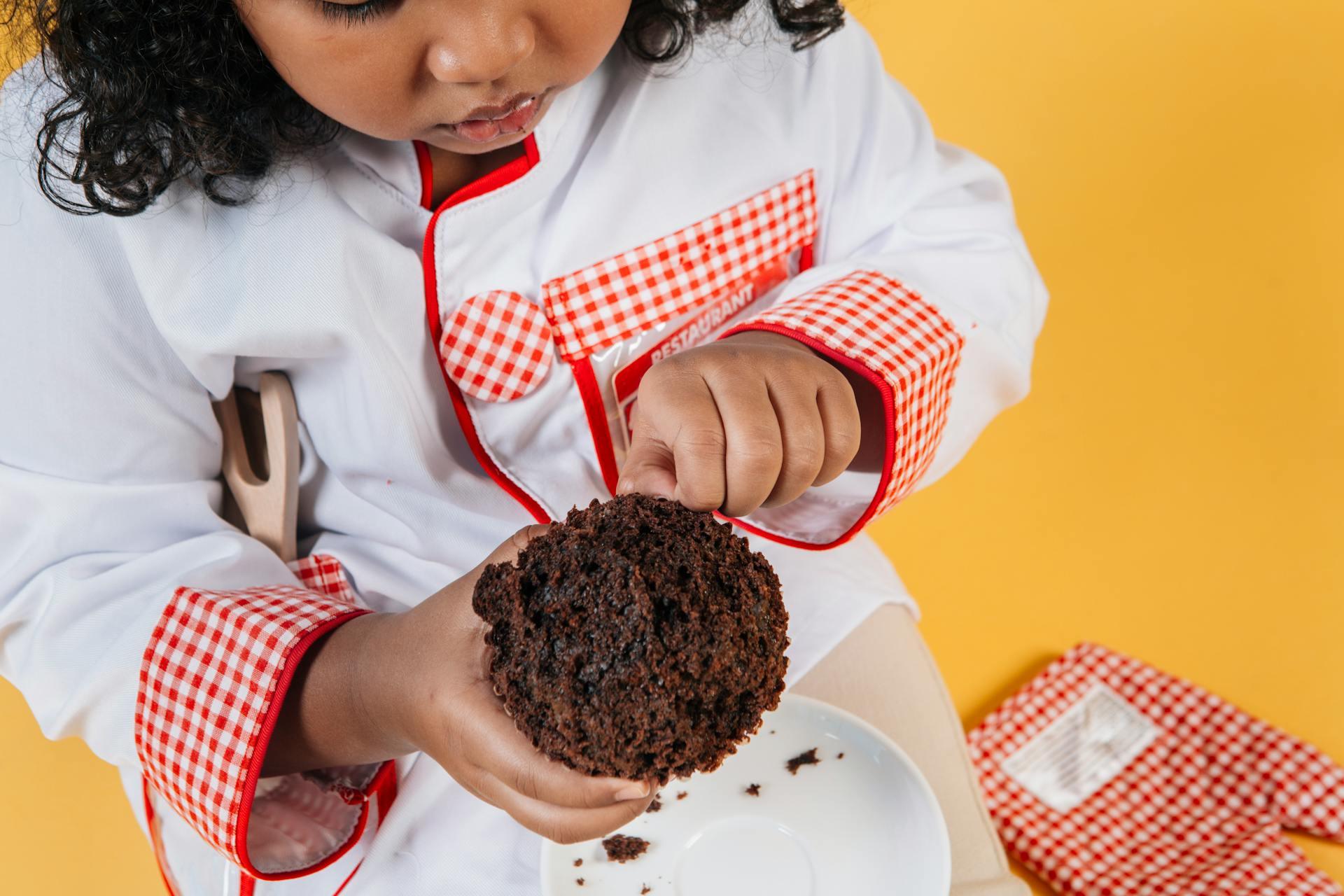 From above of crop attentive African American girl in chef uniform preparing delicious chocolate treat above saucer