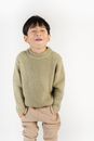 Cheerful ethnic kid in stylish apparel grimacing while looking away with hands in pockets