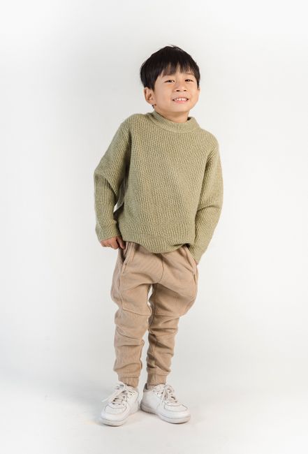 Full body of happy small ethnic adorable boy in fashionable casual outfit looking at camera on white background of studio