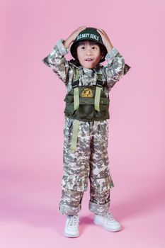 一个穿着海军海豹突击队服装的小男孩站在粉色背景前