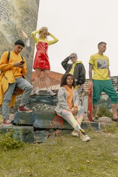 Group of stylish young adults posing in colorful outfits by urban graffiti.