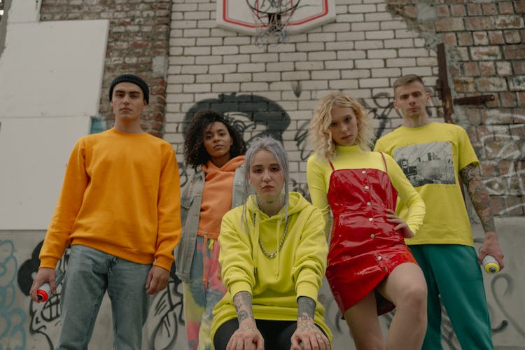 A Group Of People Standing Beside Brick Wall With Graffiti
