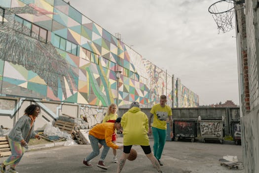 A group of diverse adults playing basketball in an urban area with graffiti.