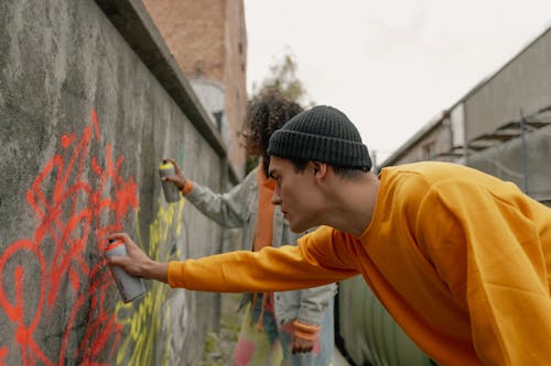 Free A Man in Yellow Sweatshirt and Knit Cap Spray Painting a Wall Stock Photo