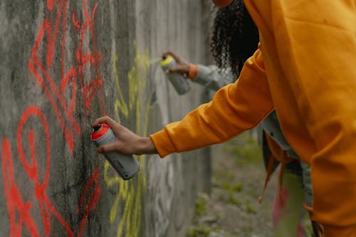 Free A Person in Yellow Long Sleeve Shirt Spray Painting a Wall Stock Photo