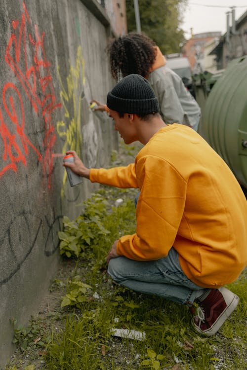 A Person in Yellow Sweatshirt and Black Knit Cap Spray Painting a Wall