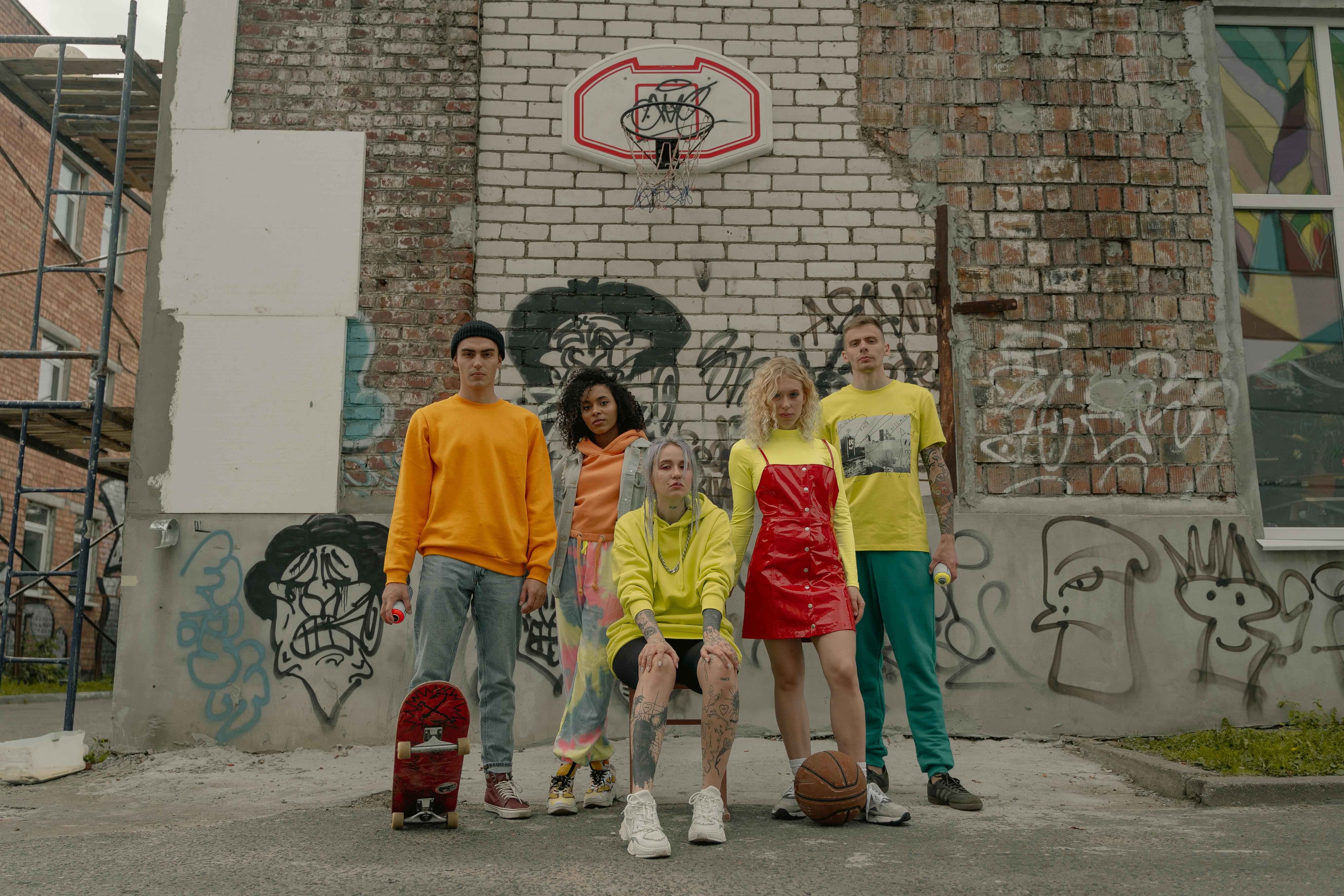 a group of people beside a wall with graffiti and a basketball ring