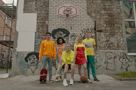 A diverse group of young adults posing in front of a graffiti-covered wall and basketball hoop.