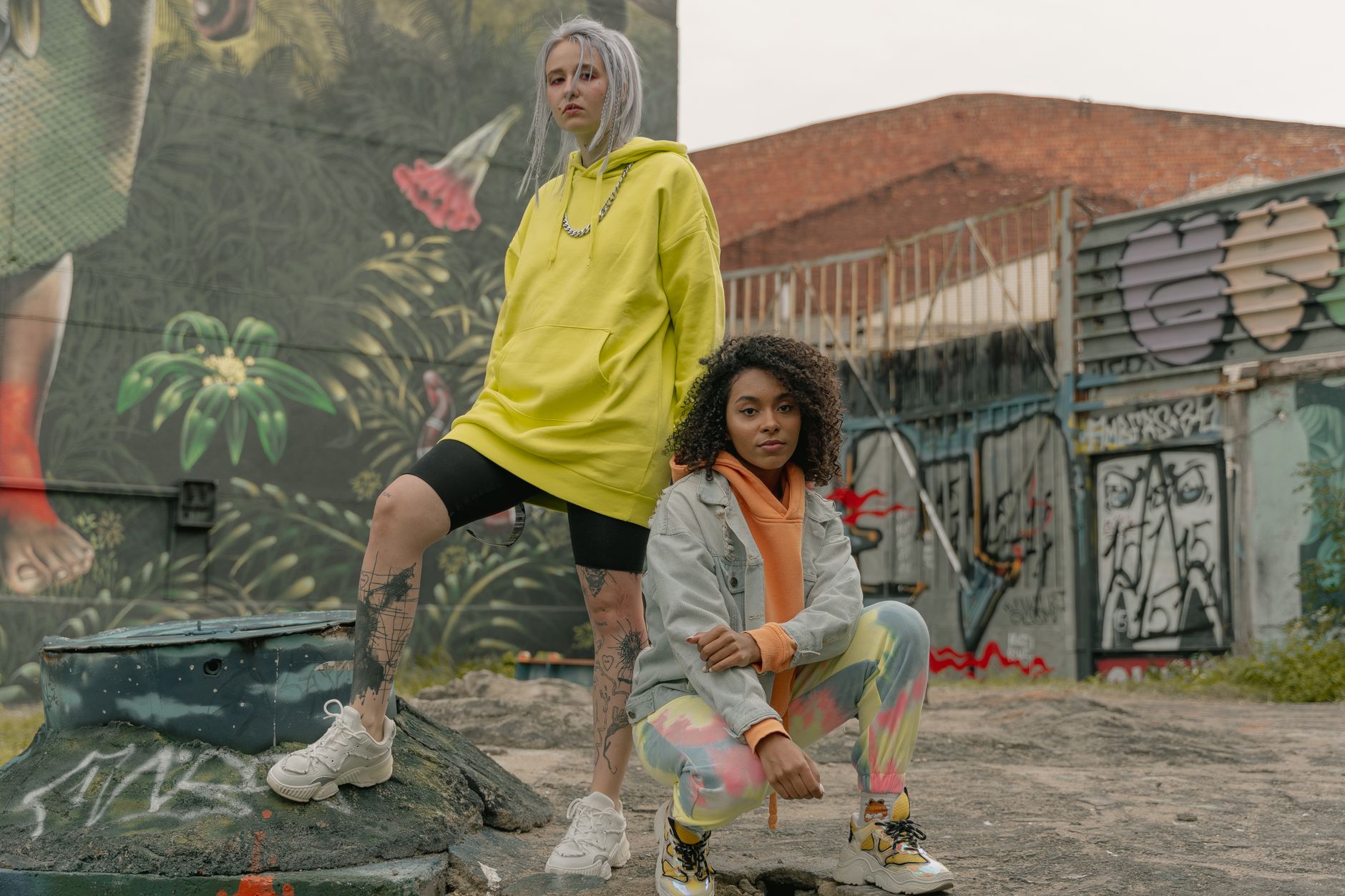 Deux femmes en hoodie jaune oversize posent devant un mur de graffitis