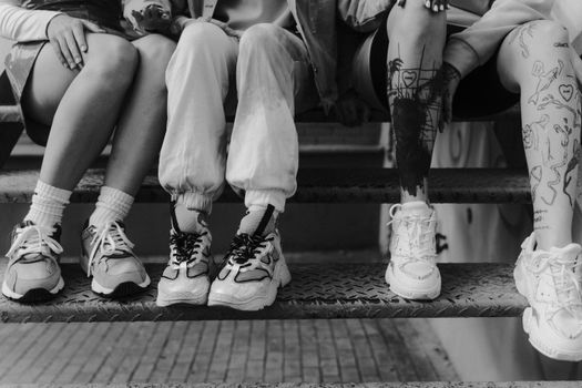 Artistic black and white photo of people sitting with focus on sneakers and tattoos.