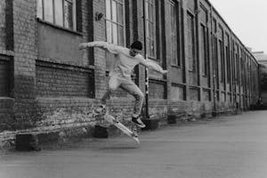 Grayscale Photo of a Man Doing a Skateboard Trick