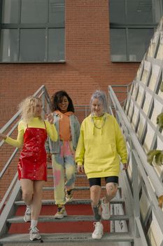 Three stylish young women walking down stairs in vibrant streetwear, showcasing modern street style.
