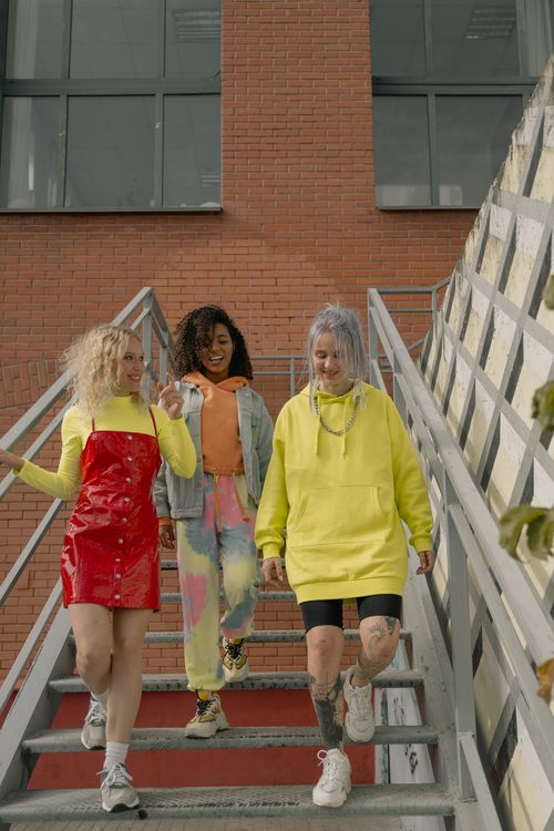 Free Three stylish young women walking down stairs in vibrant streetwear, showcasing modern street style. Stock Photo
