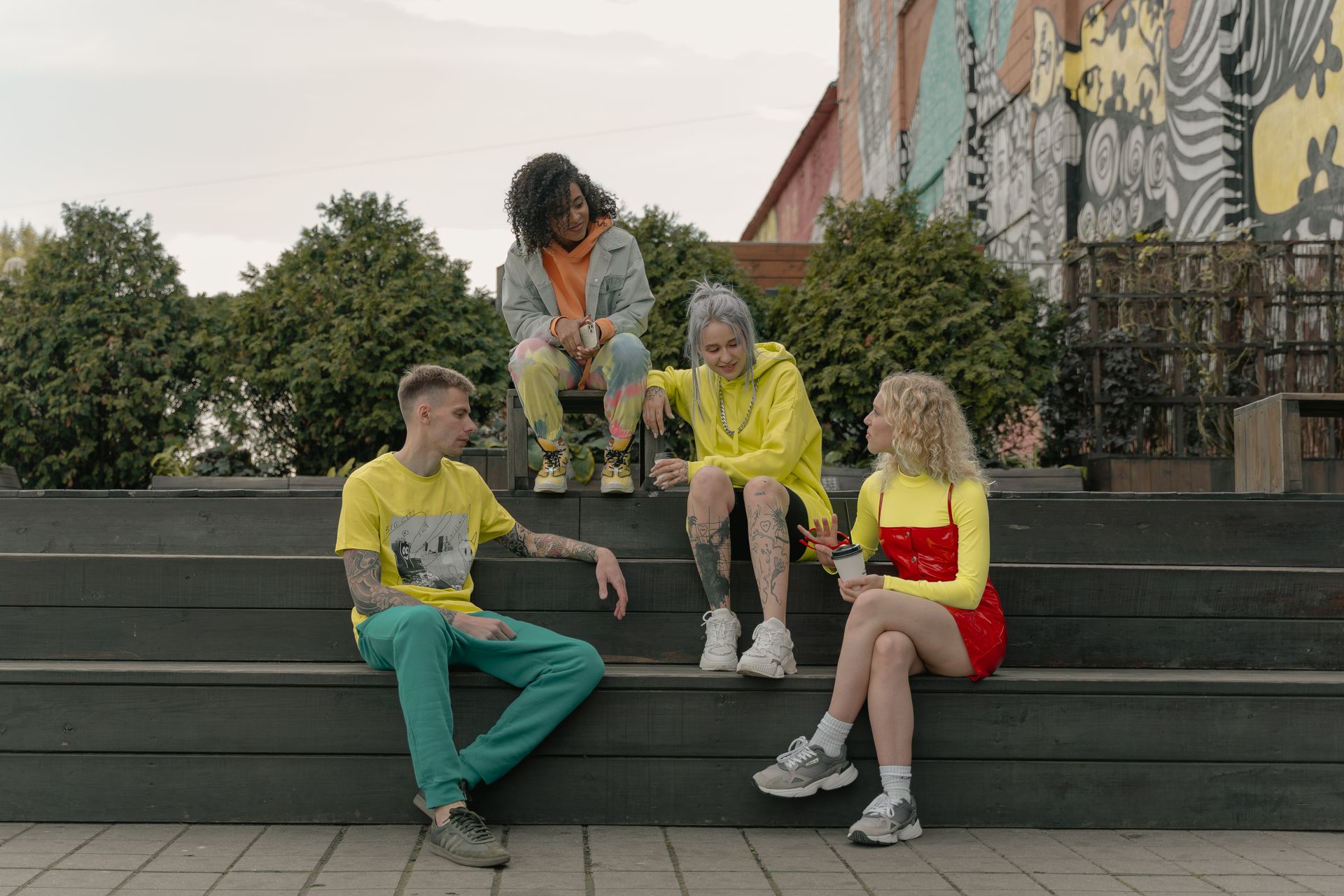 Group of young adults relaxing and chatting on steps in front of colorful street art.
