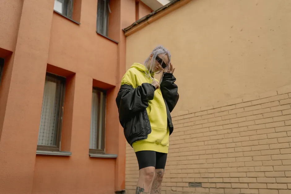 Femme portant une veste oversize noire sur un hoodie jaune, look streetwear urbain en extérieur