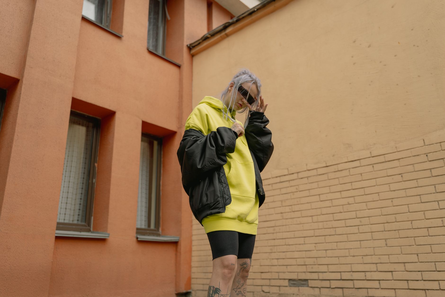 Femme portant une veste oversize noire sur un hoodie jaune, look streetwear urbain en extérieur