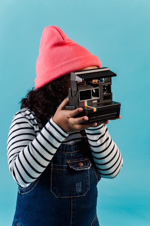 Wanita Dengan Topi Rajut Merah Memegang Kamera Polaroid Hitam Dan Abu Abu