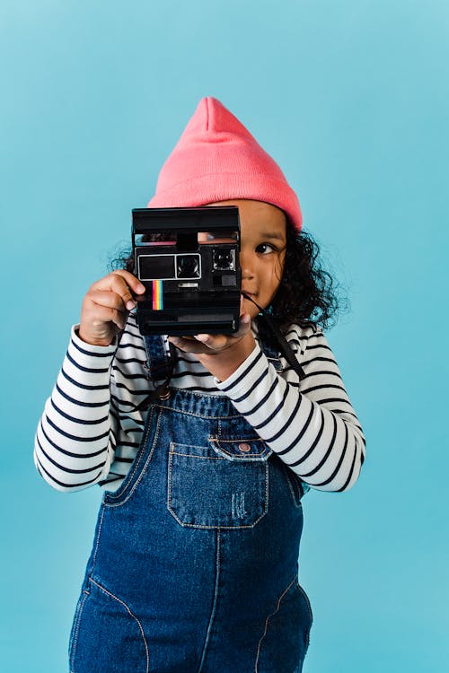 Cheerful black girl taking photo on instant camera against blue background