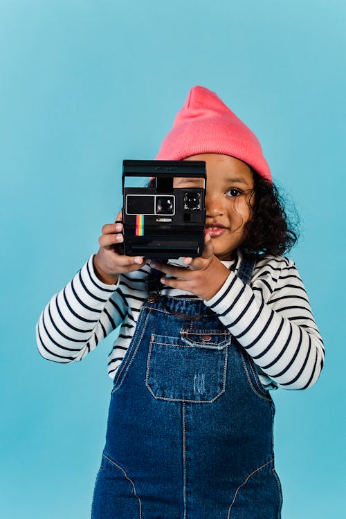 Calm black girl in stylish clothes taking picture on vintage photo camera